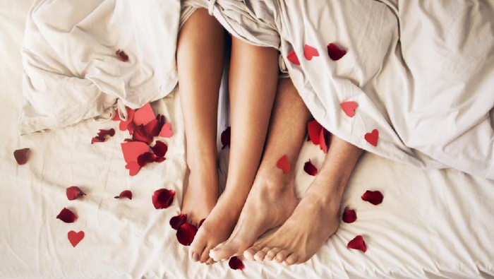 Ilustrasi Seks Shot of a couple lying under a blanket with hearts scattered on the bed