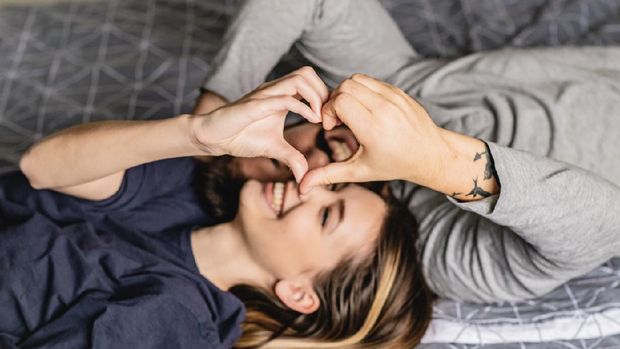 Young couple is laying in bed doing heart shape with hands