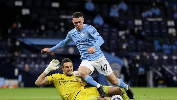 MANCHESTER, ENGLAND - MARCH 10: Phil Foden of Manchester City is challenged by Alex McCarthy of Southampton during the Premier League match between Manchester City and Southampton at Etihad Stadium on March 10, 2021 in Manchester, England. Sporting stadiums around the UK remain under strict restrictions due to the Coronavirus Pandemic as Government social distancing laws prohibit fans inside venues resulting in games being played behind closed doors. (Photo by Clive Brunskill/Getty Images)