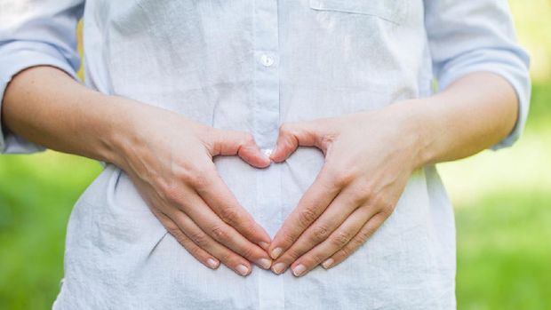 Close up picture of a pregnant woman showing a love sign on her belly in the first trimester, outdoor