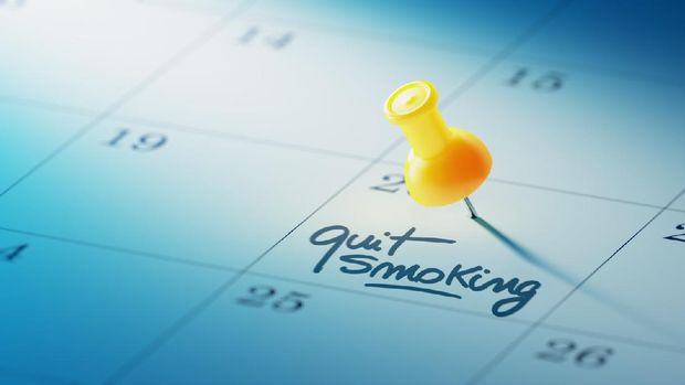 Concept image of a Calendar with a yellow push pin. Closeup shot of a thumbtack attached. The words Quit Smoking written on a white notebook to remind you an important appointment.