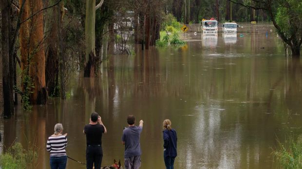 A still image taken from video shows people looking at trucks stuck in a flooded road, following heavy rains in Taree, New South Wales, Australia March 20, 2021. NSW State Emergency Service/via REUTERS   THIS IMAGE HAS BEEN SUPPLIED BY A THIRD PARTY. MANDATORY CREDIT. NO RESALES. NO ARCHIVES.