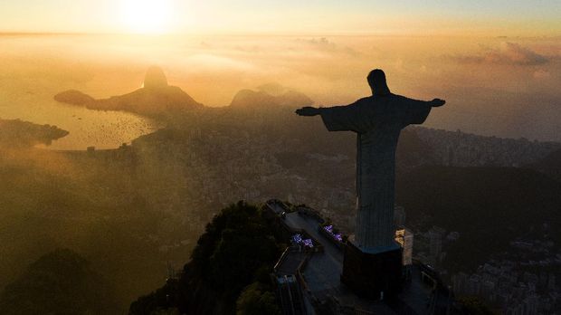 The sun rises in front of the Christ the Redeemer statue in Rio de Janeiro on March 24, 2021. - Christ the Redeemer is celebrating its 90th anniversary in October 2021 and is receiving restoration work to ensure that it looks its best for the public and visiting tourists. (Photo by CARL DE SOUZA / AFP)