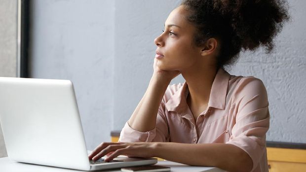 Close up portrait of a young african american woman looking out window when working on laptop