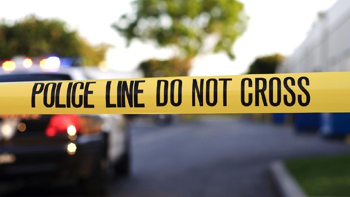 Ilustrasi garis polisi A blurred police car in the background behind yellow crime scene tape. ojol Makassar