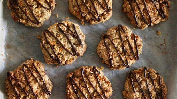 Stock photo showing an elevated view of greaseproof paper lined baking oven tray containing freshly baked, homemade carrot, coconut and chocolate chip biscuits, home baking concept.