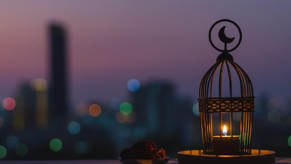 Lantern that have moon symbol on top and small plate of dates fruit with dusk sky and city bokeh light background for the Muslim feast of the holy month of Ramadan Kareem.