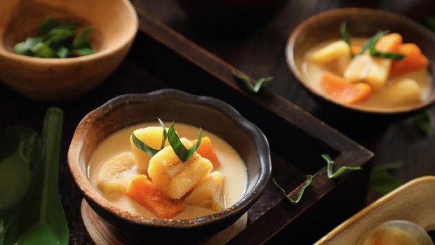 Kolak Pisang Ubi, sweet stew of plantain banana and sweet potato in coconut milk soup sweetened with palm sugar. They are served in dark-color bowls and garnished with pandan leaf cuts.