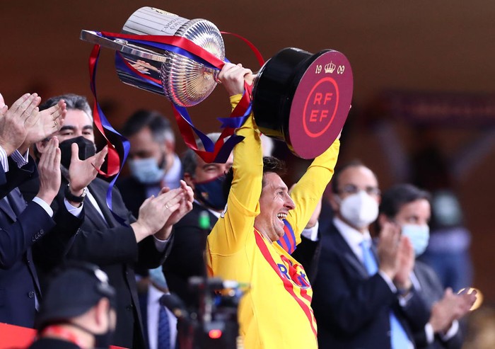 Lionel Messi Tersenyum SEVILLE, SPAIN - APRIL 17: Lionel Messi of FC Barcelona lifts the trophy after winning the Copa Del Rey Final match between Athletic Club and Barcelona at Estadio de La Cartuja on April 17, 2021 in Seville, Spain. Sporting stadiums around Spain remain under strict restrictions due to the Coronavirus Pandemic as Government social distancing laws prohibit fans inside venues resulting in games being played behind closed doors. (Photo by Fran Santiago/Getty Images)