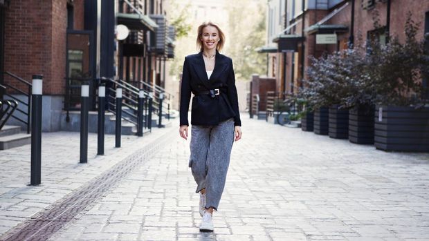 Confident Businesswoman or fashion blogger In Stylish Office Clothes walking city street. Beautiful Smiling Woman Going To Work, Wearing Style Fashionable Spring or fall black jacket, oversize slouchy jeans. Outdoors. Autumn trend