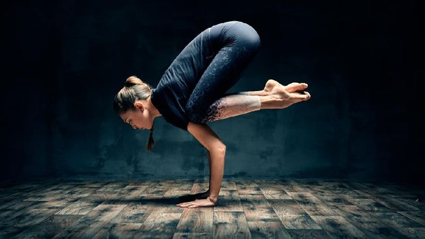 Young woman practicing yoga doing forearm stand crane pose asana in dark room. Bakasana. Wellness and healthy lifestyle