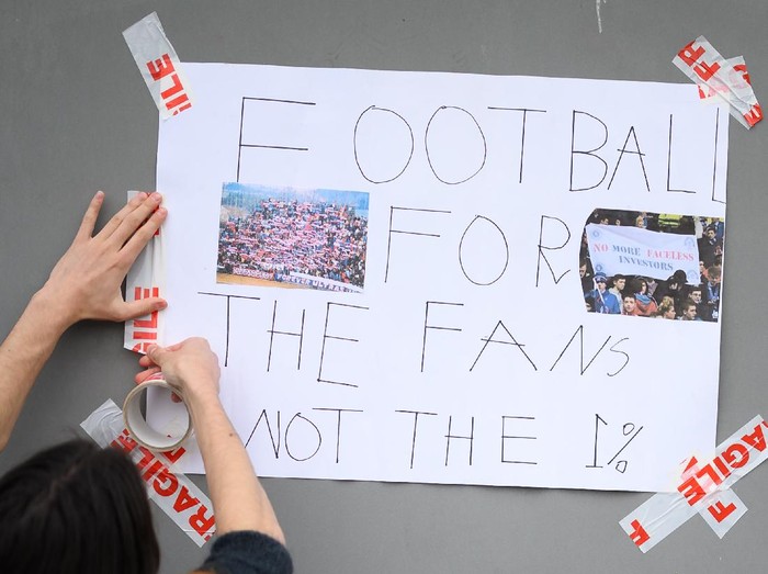 LONDON, UNITED KINGDOM - APRIL 20: Celtic fan Wolf Gillespie sticks a homemade poster protesting against the proposed European Super League to the side of Arsenal football team's Emirates Stadium on April 20, 2021 in London, United Kingdom. Six English premier league teams have announced they are part of plans for a breakaway European Super League. Arsenal, Manchester United, Manchester City, Liverpool, Chelsea and Tottenham Hotspur will join 12 other European teams in a closed league similar to that of the NFL American Football League. In a statement released last night, the new competition 