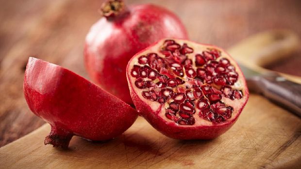Sliced pomegranate on cutting board with knife and whole pomegranate behind.  Shot with shallow focus on sliced fruit.