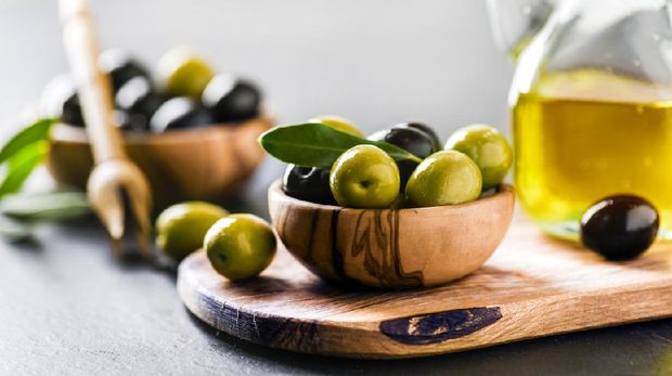 Ripe green and black olives on dark table with vigin oil in old glass bottle. Olive picker and leaves on wooden board.