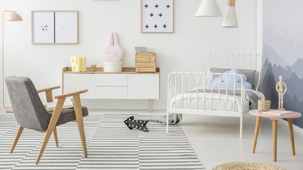 Pink table and grey wooden armchair in girl's bedroom interior with mockup of empty poster