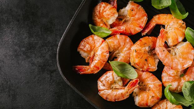 Fried grilled prawns with fresh herbs and basil on grill pan on dark background. Top view with place for text