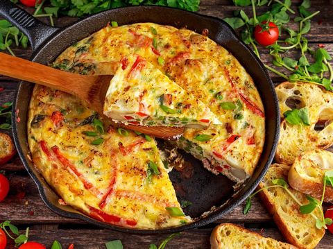 Frittata made of eggs, potato, bacon, paprika, parsley, green peas, onion, cheese in iron pan on wooden table