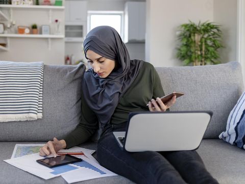 Focused Young Muslim Female Entrepreneur Wearing a Hijab Reading Through Paperwork While Working in Her Home Office. Work Opportunities For Muslim Women Concept. Freelance Concept.