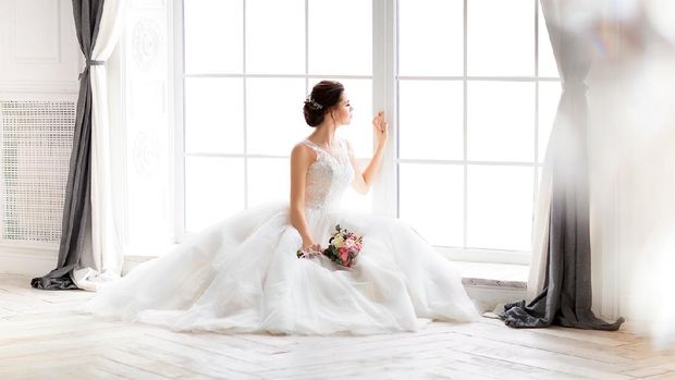 Young beautiful brunette woman with bouquet posing in a wedding dress