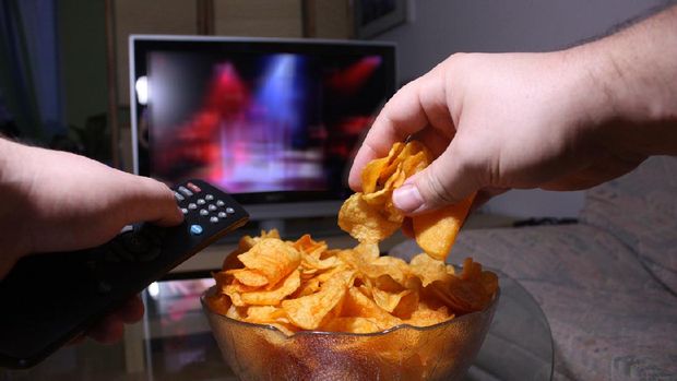 Relaxing and watching TV on the couch while eating chips.