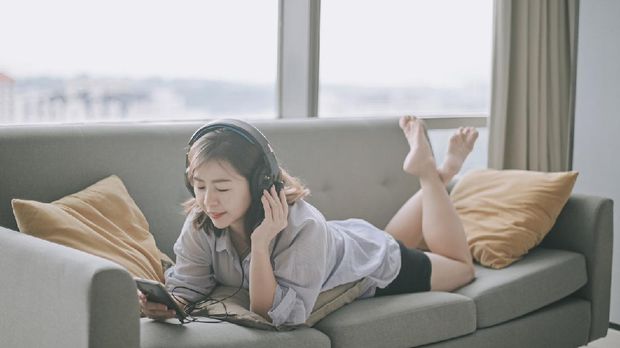 asian chinese beautiful woman enjoy ME time at home during weekend listening to music on sofa with her smart phone and headphone