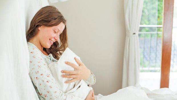 Woman sitting in a white bedroom with little child and smiling