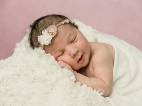 bayi perempuan Sleeping newborn baby girl laying on a cream colored blanket on a pink purple backdrop with a headband in her hair and a slight smile