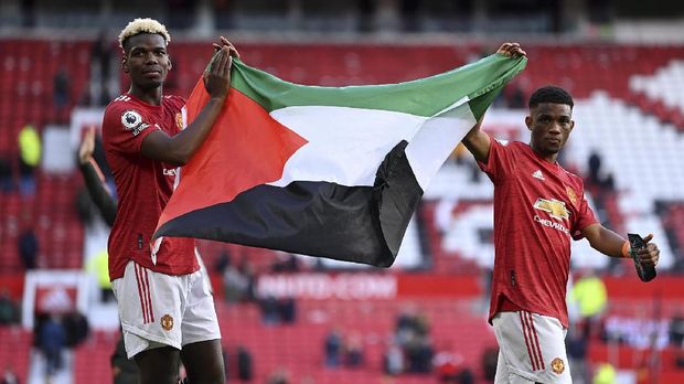 Soccer Football - Premier League - Manchester United v Fulham - Old Trafford, Manchester, Britain - May 18, 2021 Manchester United's Paul Pogba applauds fans while holding a Palestinian flag with Amad Diallo during a lap of appreciation after the match Pool via REUTERS/Laurence Griffiths EDITORIAL USE ONLY. No use with unauthorized audio, video, data, fixture lists, club/league logos or 'live' services. Online in-match use limited to 75 images, no video emulation. No use in betting, games or single club /league/player publications. Please contact your account representative for further details.