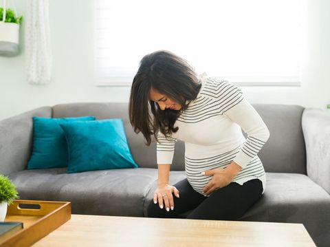 Caucasian pregnant woman having contractions at home and about to go into a labor. Expectant mother beggining to have contractions in the sofa