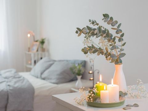 burning candles and eucalyptus in  vase in white bedroom