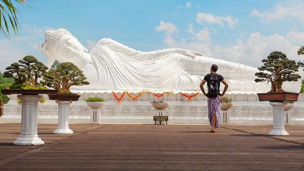 Vihara Dharma Giri Young man travel in Bali, Indonesia. Tourist walk in buddhist temple Vihara Dharma Giri, see at lying Buddha statue. Popular travel destination background. Art, culture, religions of Indonesian people