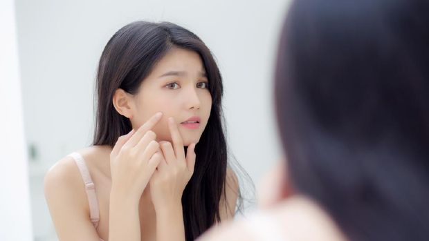 Beautiful young asian woman looking the mirror and touch face is a acne, zit treatment, beauty girl problem beauty and skin with wrinkled on facial in the room at home, makeup and cosmetic concept.