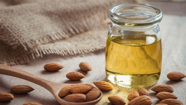 Almond oil in glass bottle and almonds on wooden table