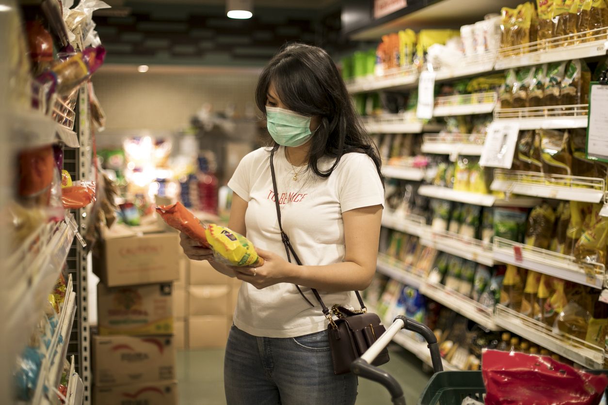 Asian young woman shopping in a grocery store and wearing protective medical mask during social distances and lockdown due to coronavirus