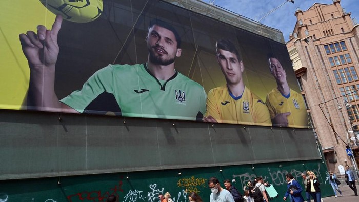 Passers-by walk past a billboard depicting players of the Ukrainian national football team, in Kiev on June 7, 2021. - Ukraine provoked Moscows ire Sunday as its football federation unveiled Euro 2020 kits that feature Russian-annexed Crimea and popular nationalist slogans. The Union of European Football Associations has approved a new uniform for the Ukrainian national football team for the 2020 European Championship, which depicts the borders of the republic, including Crimea. (Photo by Sergei SUPINSKY / AFP)