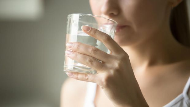 A woman drinks from a glass of water.  Image of health care, lifestyle, close up