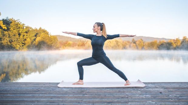 Shot of young woman doing yoga in nature on a misty morning in Ljubljana, Slovenia. Foggy lake is in the back.