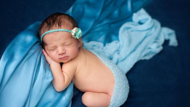 The newborn was wrapped in a green cloth and was placed on a soft rubber mat with a blurred background.