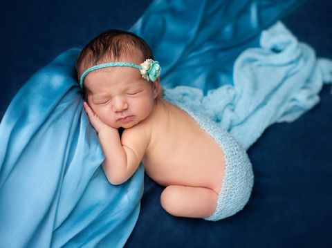 The newborn was wrapped in a green cloth and was placed on a soft rubber mat with a blurred background.