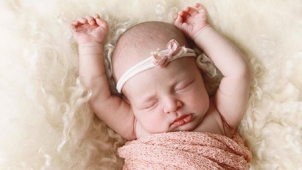 The newborn was wrapped in a green cloth and was placed on a soft rubber mat with a blurred background.