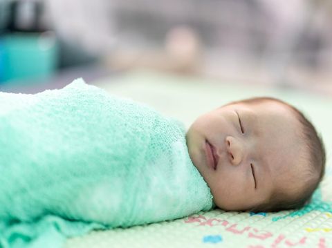 bayi perempuan The newborn was wrapped in a green cloth and was placed on a soft rubber mat with a blurred background.