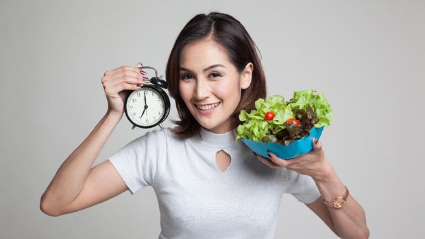 Young Asian woman with clock and salad on gray background