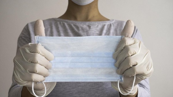 Woman with hands in latex glove holding protective medical white mask.