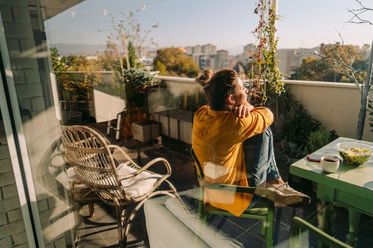 Photo of a woman drinking first morning coffee, eating 'take out' food and reading daily news online - on the balcony of her apartment while enjoying springtime sun