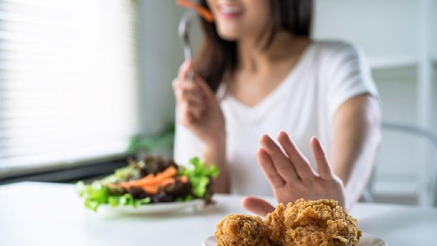 Woman on dieting for good health concept, young women use hands to push fried chicken and choose to eat vegetables for good health.