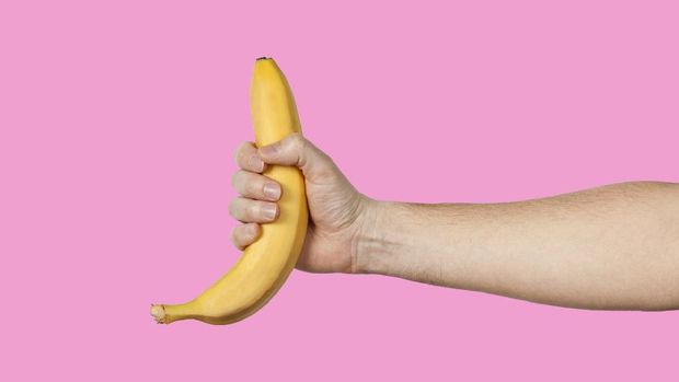Banana as a symbol of the male penis in the hand on the yellow color that is hidden by identification.  Sexual masturbation and ejaculation, impotence problem.  The goal of personal well-being.