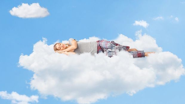 Tranquil scene of a young woman dreaming and sleeping on a cloud up in the sky