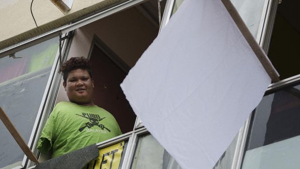 Warga Malaysia Kibarkan Bendera Putih Untuk Minta Bantuan Mohamad Nor Abdullah, born without arms, looks out from a window near a white flag outside the window of his rented room in Kuala Lumpur, Malaysia on July 3, 2021. When Mohamad Nor put a white flag outside his window late at night, he didn’t expect the swift outpouring of support. By morning, dozens of strangers knocked on his door, offering food, cash and encouragement. (AP Photo/Vincent Thian)