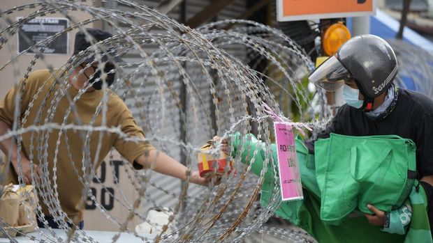 A resident, left, receives food from a delivery man through barbwire at Segambut Dalam area placed under the enhanced movement control order (EMCO) due to drastic increase in the number of COVID-19 cases recorded in Kuala Lumpur, Malaysia, Sunday, July 4, 2021. Malaysia starts further tightening movement curbs and imposes a curfew in most areas in its richest state Selangor and parts of Kuala Lumpur, where coronavirus cases remain high despite a national lockdown last month. (AP Photo/Vincent Thian)