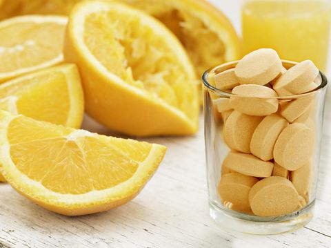 A close up shot of sliced and squeezed oranges a glass of orange juice and a glass full of orange flavored vitamin C Pills. Eat the orange, drink the juice or take a pill.